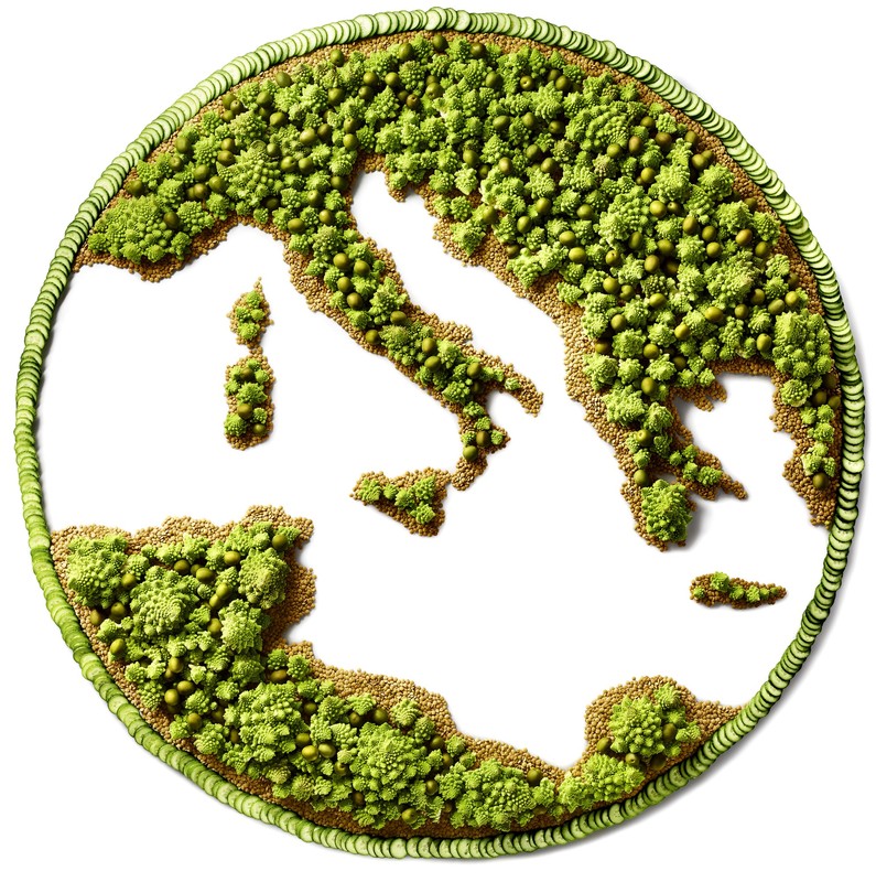 Overhead shot of a food map of Italy, made from vegetables: green Romanesco broccoli, cucumbers, and couscous on a white backdrop.