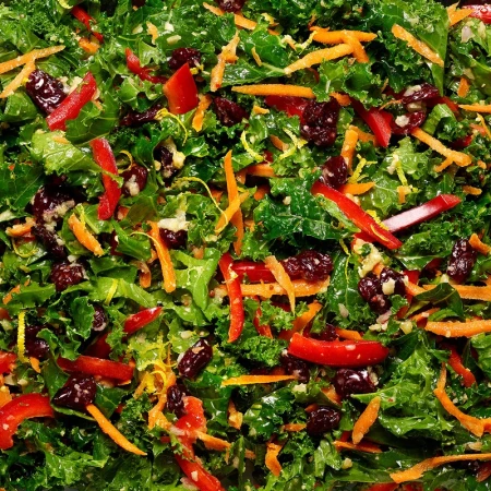Overhead shot of a vibrant kale salad with shredded carrots, red bell peppers, and dried cranberries, showcasing fresh ingredients.