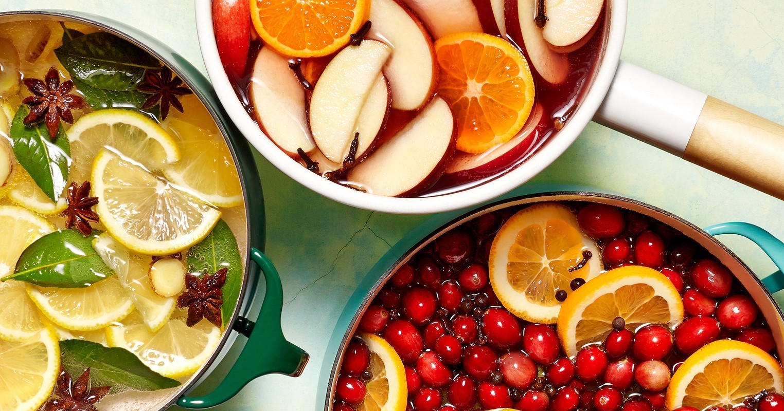 Overhead shot of three pots filled with cranberries, lemons, and oranges. The fruits are infused in liquid.