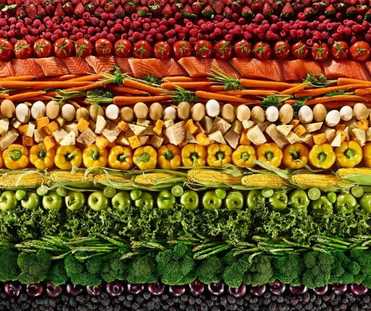 Overhead shot of rows of colourful fruits and vegetables, including berries, tomatoes, salmon, carrots, eggs, cheese, corn, apples, and lettuce.