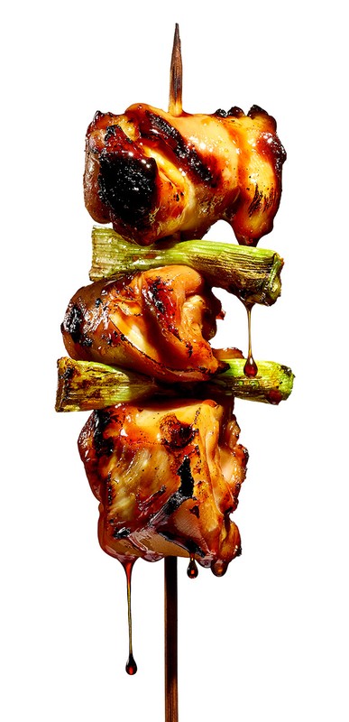 Skewered chicken and scallions, grilled and glazed, stacked on a wooden skewer. The food photography features dramatic lighting.