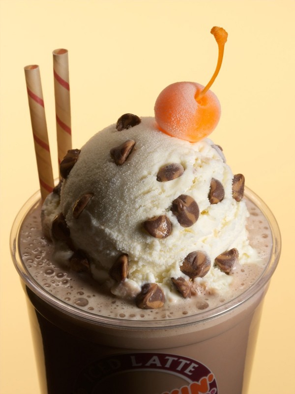 Chocolate latte with ice cream, chocolate chips, cherry, and straws. Close-up of a sweet, creamy dessert drink in a plastic cup.