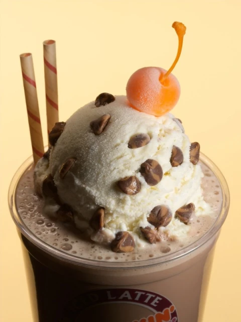 Chocolate latte with ice cream, chocolate chips, cherry, and straws. Close-up of a sweet, creamy dessert drink in a plastic cup.