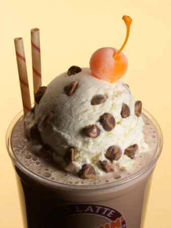 Chocolate latte with ice cream, chocolate chips, cherry, and straws. Close-up of a sweet, creamy dessert drink in a plastic cup.