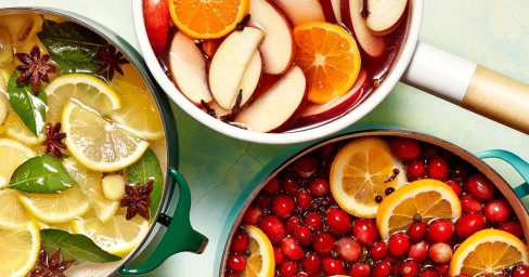 Top-down view of three pots filled with colorful infusions of citrus slices, cranberries, and spices styled by Brett Kurzweil.