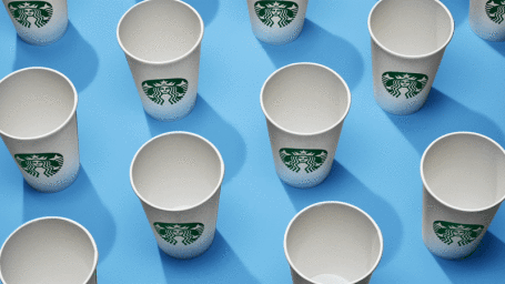 An overhead arrangement of white paper Starbucks coffee cups casting sharp shadows on a bright blue background.