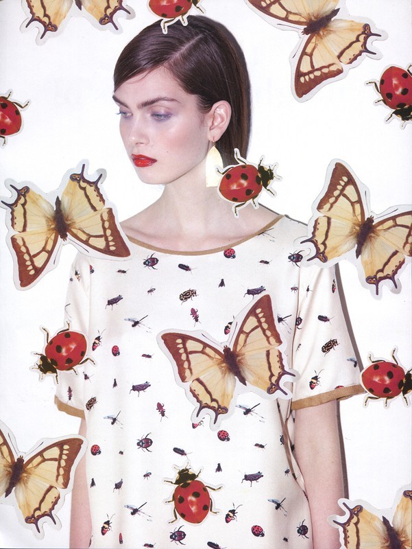 Fashion editorial shot of a woman in a patterned blouse surrounded by butterfly and ladybug stickers against a bright white backdrop.