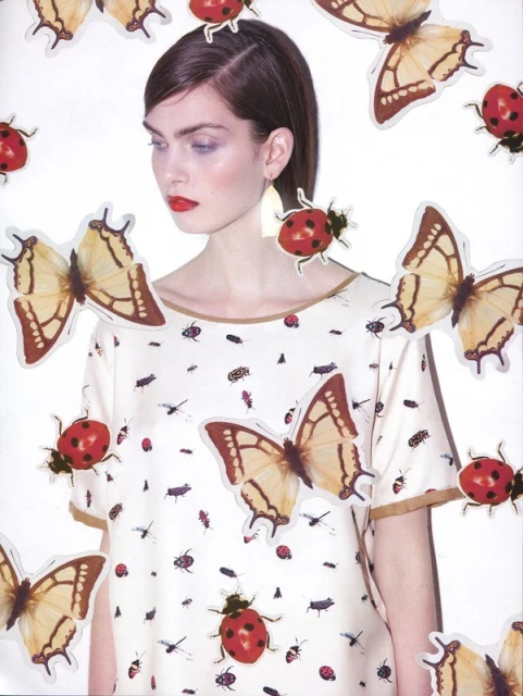 Fashion editorial shot of a woman in a patterned blouse surrounded by butterfly and ladybug stickers against a bright white backdrop.