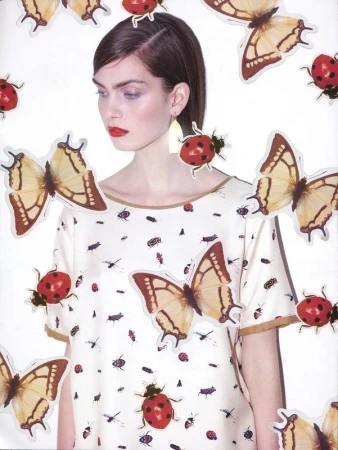 Fashion editorial shot of a woman in a patterned blouse surrounded by butterfly and ladybug stickers against a bright white backdrop.