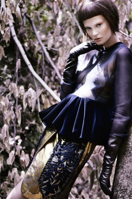 A poised fashion model in haute couture stands against a tree, showcasing an avant-garde aesthetic with structured fabric and striking lines.