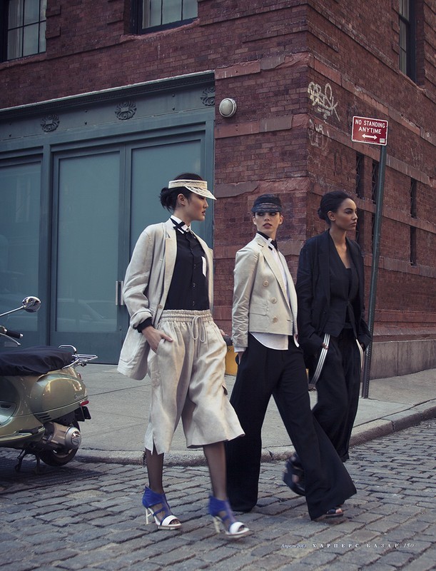 Three women pose outdoors on a city street in blazers, button-down shirts, and trousers, next to a scooter, urban fashion editorial.