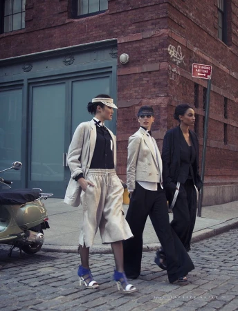 Three women pose outdoors on a city street in blazers, button-down shirts, and trousers, next to a scooter, urban fashion editorial.