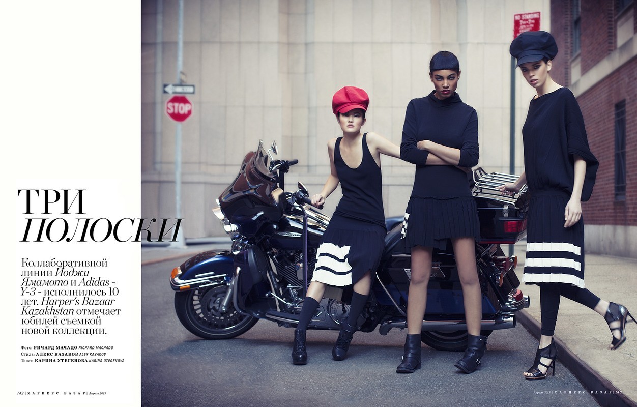 Three fashion models in black outfits pose next to a motorcycle on a city street, showcasing a blend of urban style and edgy fashion.