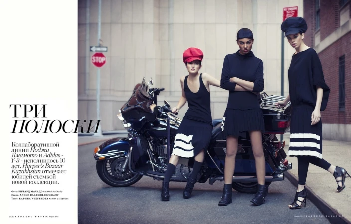 Three fashion models in black outfits pose next to a motorcycle on a city street, showcasing a blend of urban style and edgy fashion.