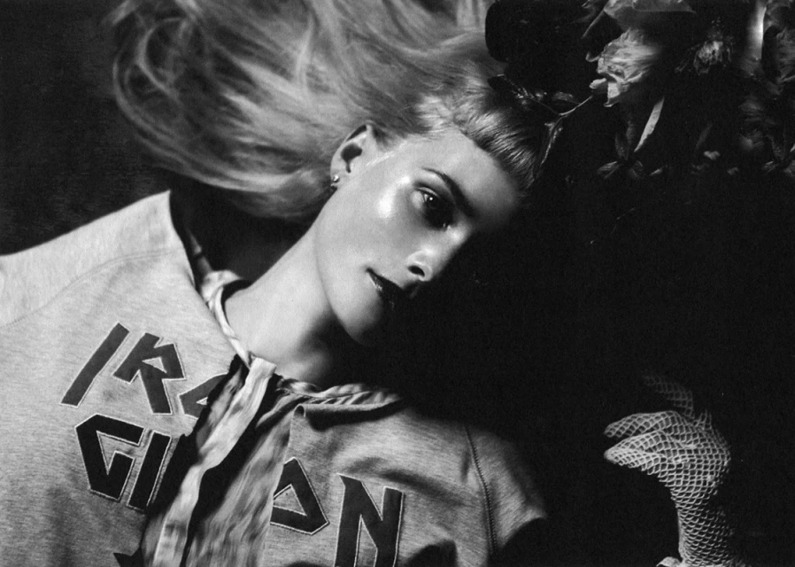 Black and white portrait of a blonde adult female wearing a hooded sweatshirt with floral elements over a dark background.