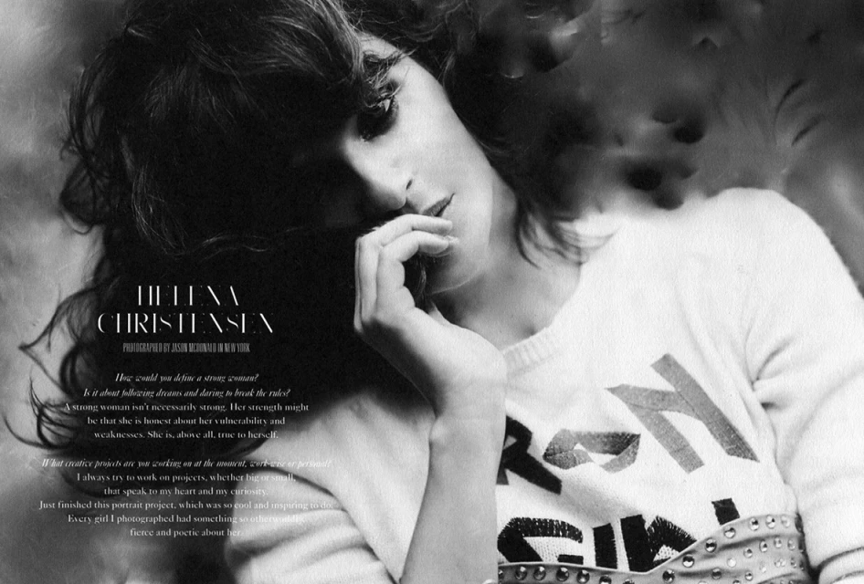 Black-and-white portrait of Helena Christensen wearing a printed sweater, her fingers to her lips in an indoor setting.