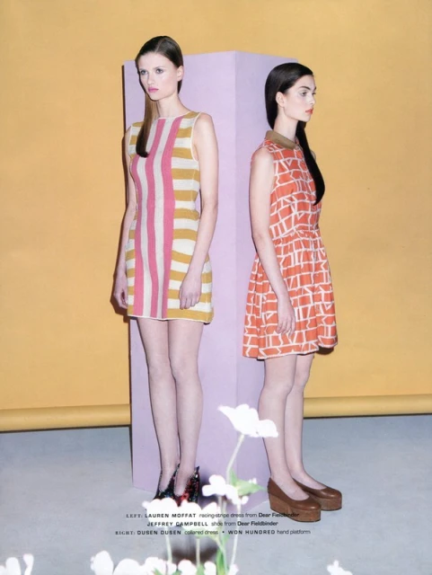 Two fashion models pose in colorful dresses against a yellow and lavender backdrop, showcasing a vintage-inspired aesthetic.