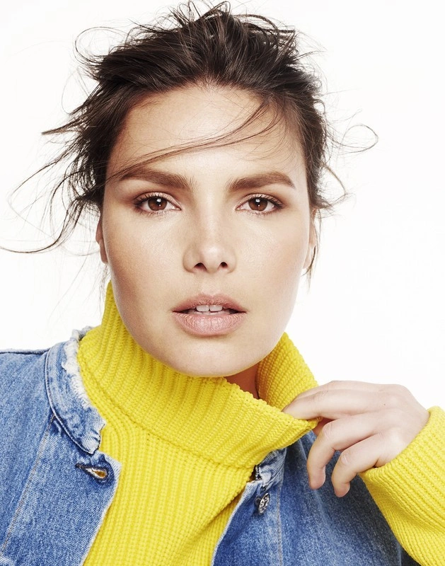 Close-up portrait of a woman wearing a vibrant yellow turtleneck and denim jacket against a white background