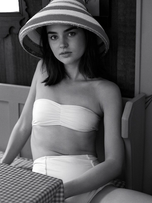 Monochrome portrait of a woman wearing a wide-brimmed striped hat and a bandeau bikini top while seated indoors