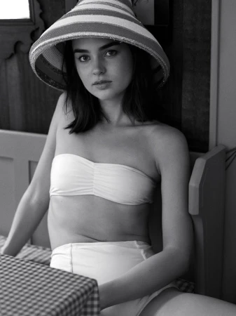 Monochrome portrait of a woman wearing a wide-brimmed striped hat and a bandeau bikini top while seated indoors
