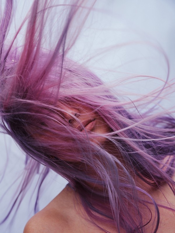 Close-up of an adult woman with purple hair blowing, with focus on hair texture, color, and visible facial features.