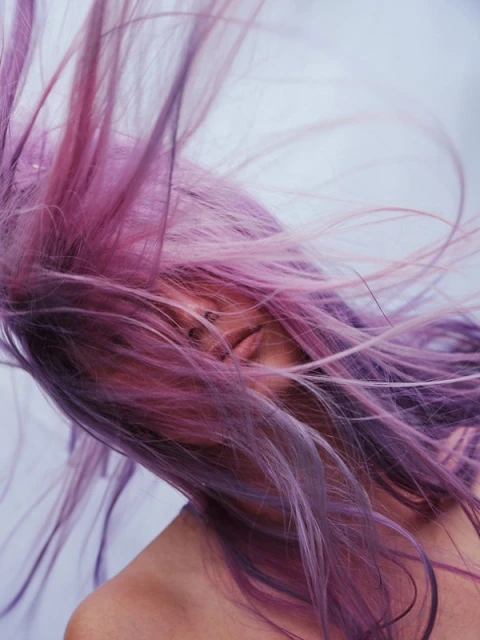 Close-up of an adult woman with purple hair blowing, with focus on hair texture, color, and visible facial features.