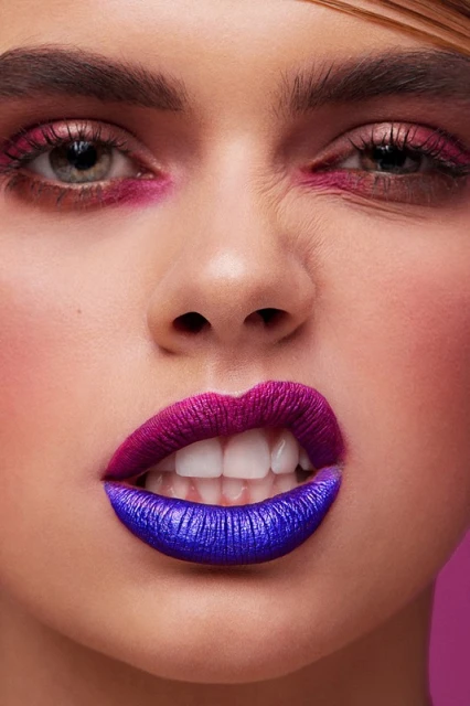 Close-up portrait of a woman with creative makeup. Her lips are painted with a duo-tone of purple and blue lipstick with pink eyeshadow.