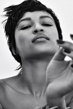 Close-up monochrome portrait of a woman with short dark hair looking down towards the camera with hand raised in the foreground.