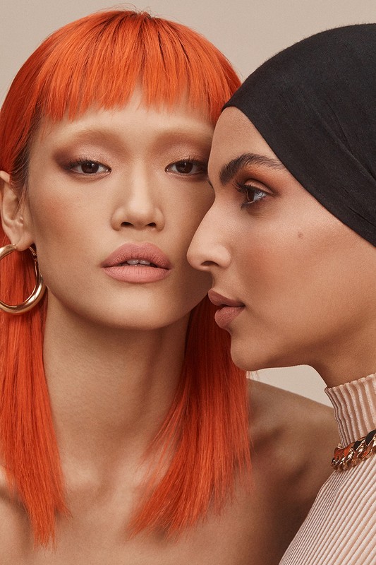 Close-up portrait of two diverse adult women with styled makeup and headwear in a beauty shot for fashion or beauty industries.