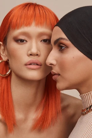 Close-up portrait of two diverse adult women with styled makeup and headwear in a beauty shot for fashion or beauty industries.