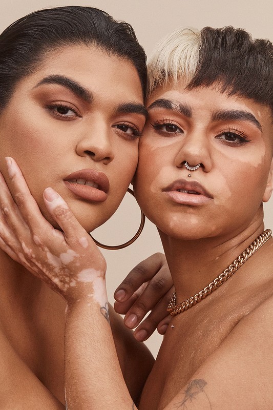 Close-up portrait of two adult females with unique skin tones, fair and dark hair, gold jewellery in a studio setting. Beauty and diversity.