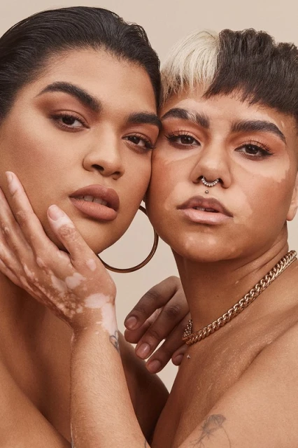 Close-up portrait of two adult females with unique skin tones, fair and dark hair, gold jewellery in a studio setting. Beauty and diversity.