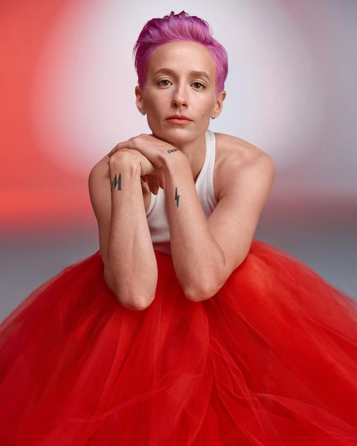 Portrait of an adult female with short pink hair, wearing a white top and a large red tulle skirt, with a neutral facial expression.