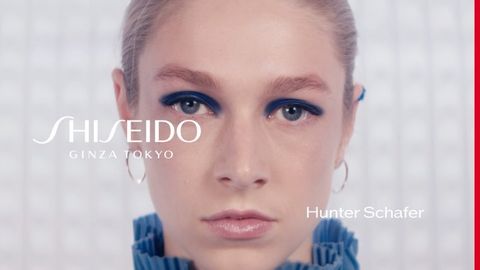 Close-up beauty shot of Hunter Schafer wearing blue eyeshadow and hoop earrings.  Branding includes Shiseido Ginza Tokyo.