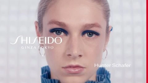 Close-up beauty shot of Hunter Schafer wearing blue eyeshadow and hoop earrings.  Branding includes Shiseido Ginza Tokyo.