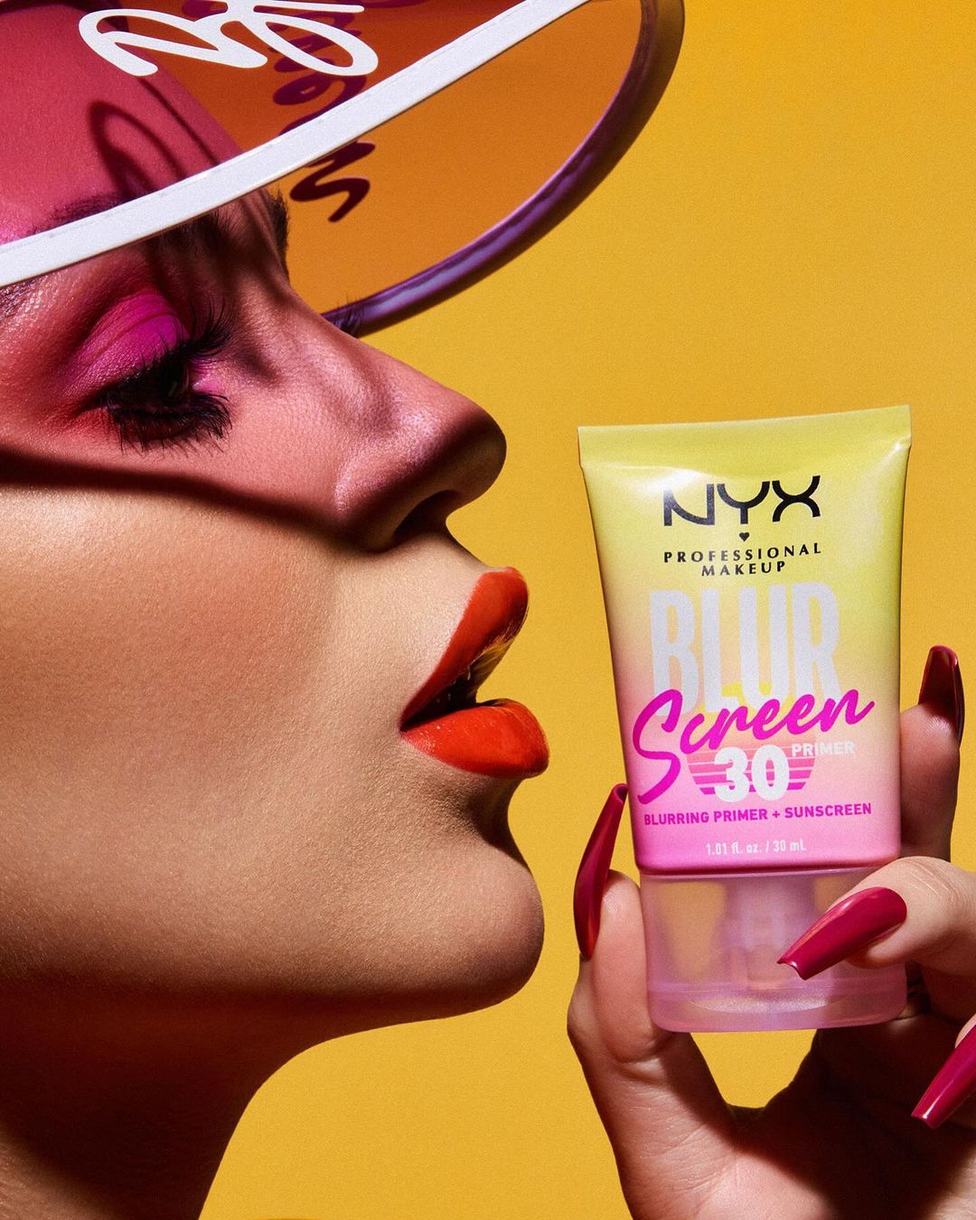 Woman with bright makeup and visor holds NYX Blur Screen Primer. The cosmetic product is prominently displayed against a yellow backdrop.