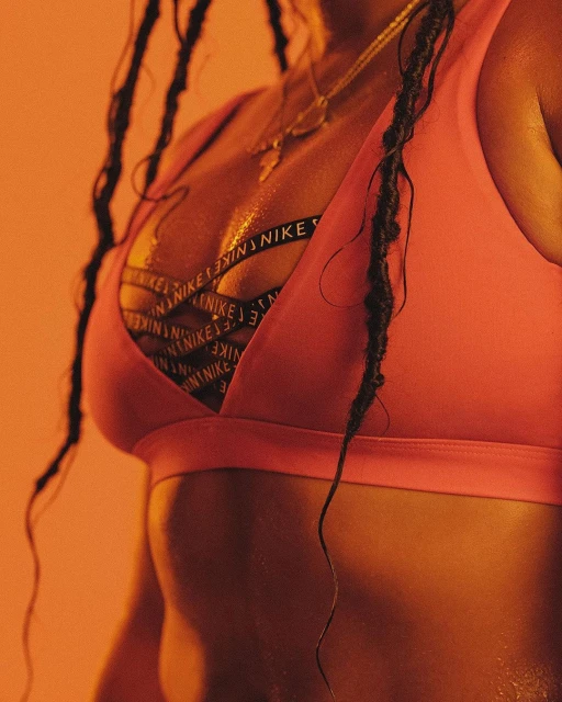 Close-up shot of a fit African American woman wearing a pink sports bra with black Nike straps, jewelry, and braided hair.