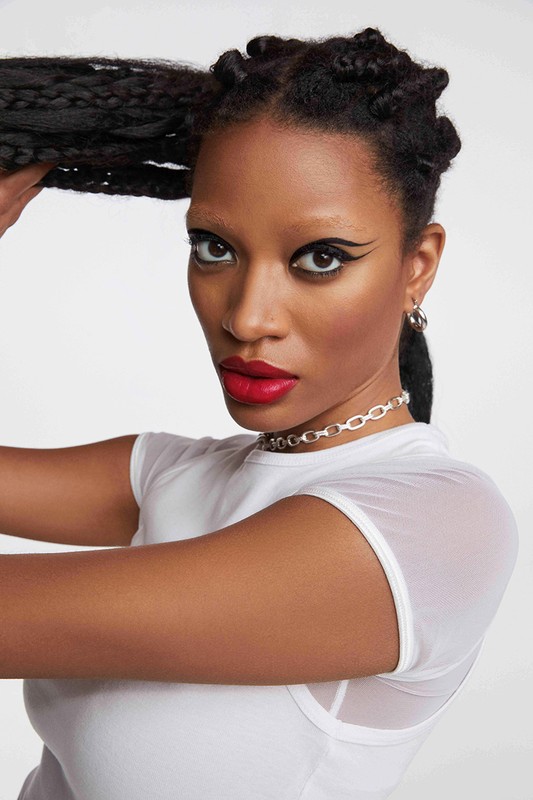 Close-up portrait of a Black woman with braided hair wearing a white top, bold red lipstick, and winged eyeliner.