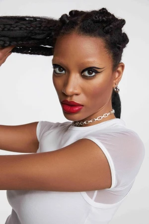 Close-up portrait of a Black woman with braided hair wearing a white top, bold red lipstick, and winged eyeliner.