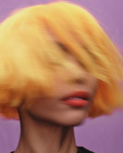 Close-up portrait of an adult female with orange short hair and coral lipstick, set against a solid purple backdrop, motion blurred.