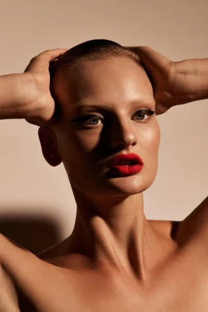 Close-up portrait of a woman with slicked-back hair, winged eyeliner, and vibrant red lipstick holding her hands behind her head.