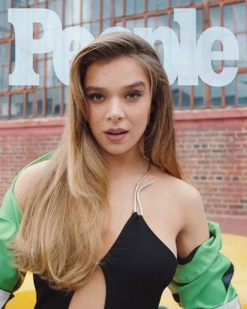 Hailee Steinfeld wearing a black top and green jacket with a brick building background photographed by Brooke Nipar