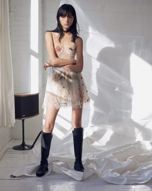 Fashionable young woman poses in a mini dress and black boots in a photo studio with natural light, capturing her style and confidence.