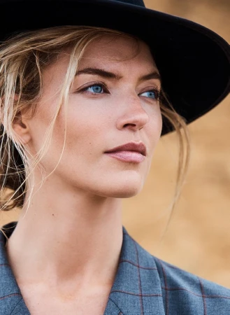 Close-up portrait of a woman with blonde hair wearing a black hat and blue patterned jacket outdoors in Los Angeles