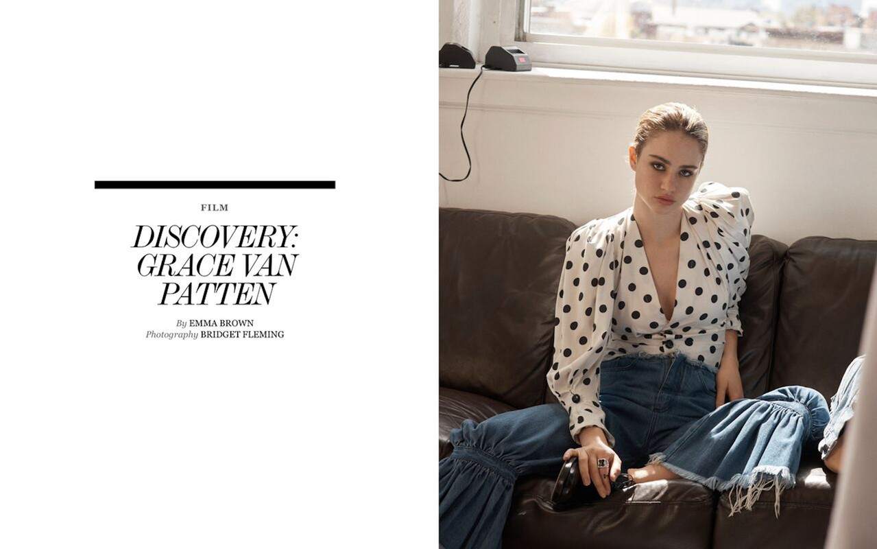 Woman in polka dot blouse and jeans sits on leather couch in window light in a fashion editorial, shot in a lifestyle setting.