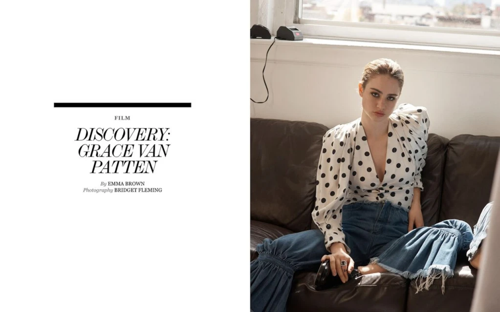 Woman in polka dot blouse and jeans sits on leather couch in window light in a fashion editorial, shot in a lifestyle setting.