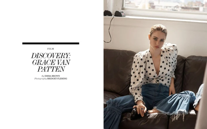 Woman in polka dot blouse and jeans sits on leather couch in window light in a fashion editorial, shot in a lifestyle setting.