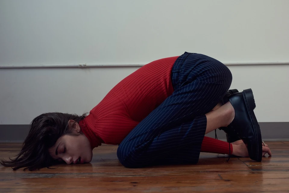 Outdoor portrait of an adult male model in a brown sweater, standing against a concrete wall with dappled sunlight.