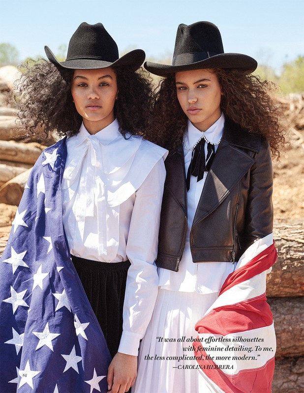 Two models wearing black cowboy hats and white blouses with American flags wrapped around them in a wooded clearing.