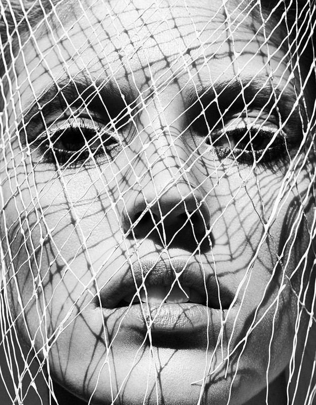 Black and white portrait of a woman's face partially obscured by a netting material, showcasing a blend of texture and shadow play.